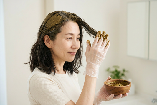 自宅で手袋を着け、木の器のヘナペーストを髪に塗る女性